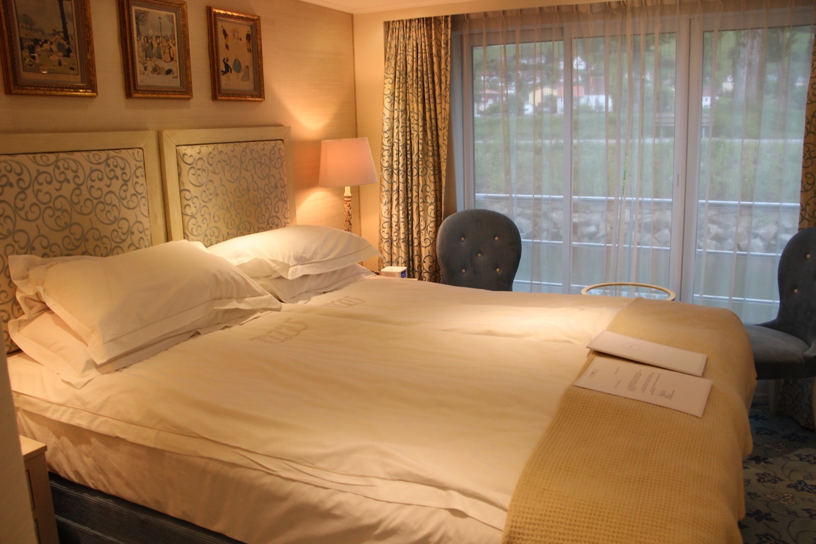 A river cruise cabin with a bed beside a floor-to-ceiling French-balcony window.