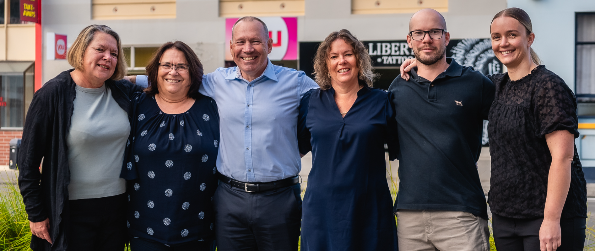 You Travel Napier team standing together in front of their offices smiling at camera, arms around each other