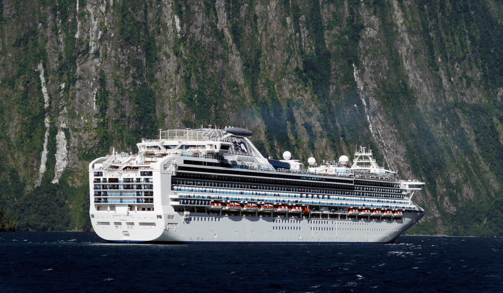 A cruise ship dwarfed by the sheer cliffs of Milford Sound, New Zealand.