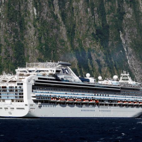 A cruise ship dwarfed by the sheer cliffs of Milford Sound, New Zealand.