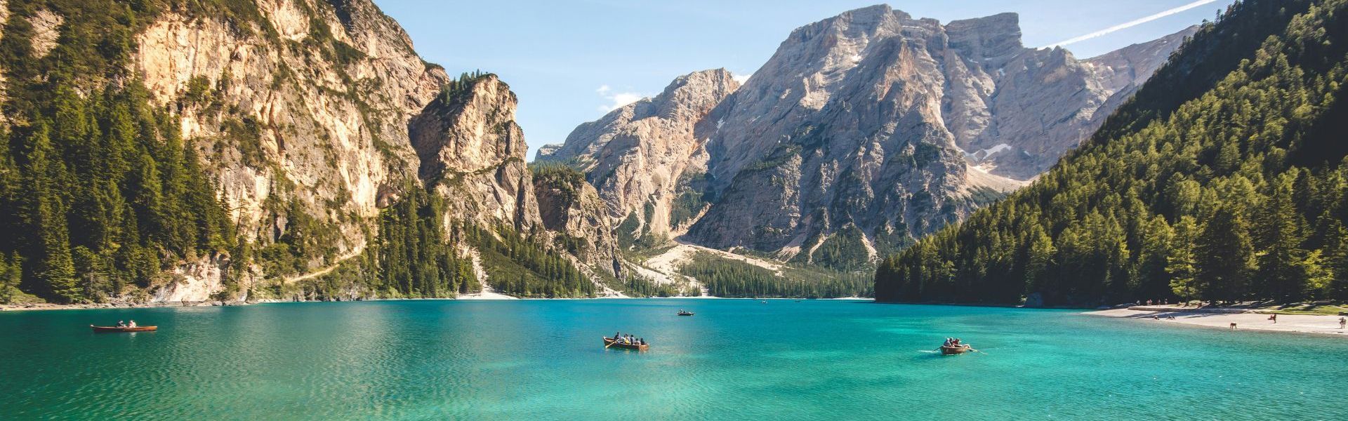 tourists sit in small row boats on an emerald green lake in the mountains of italy